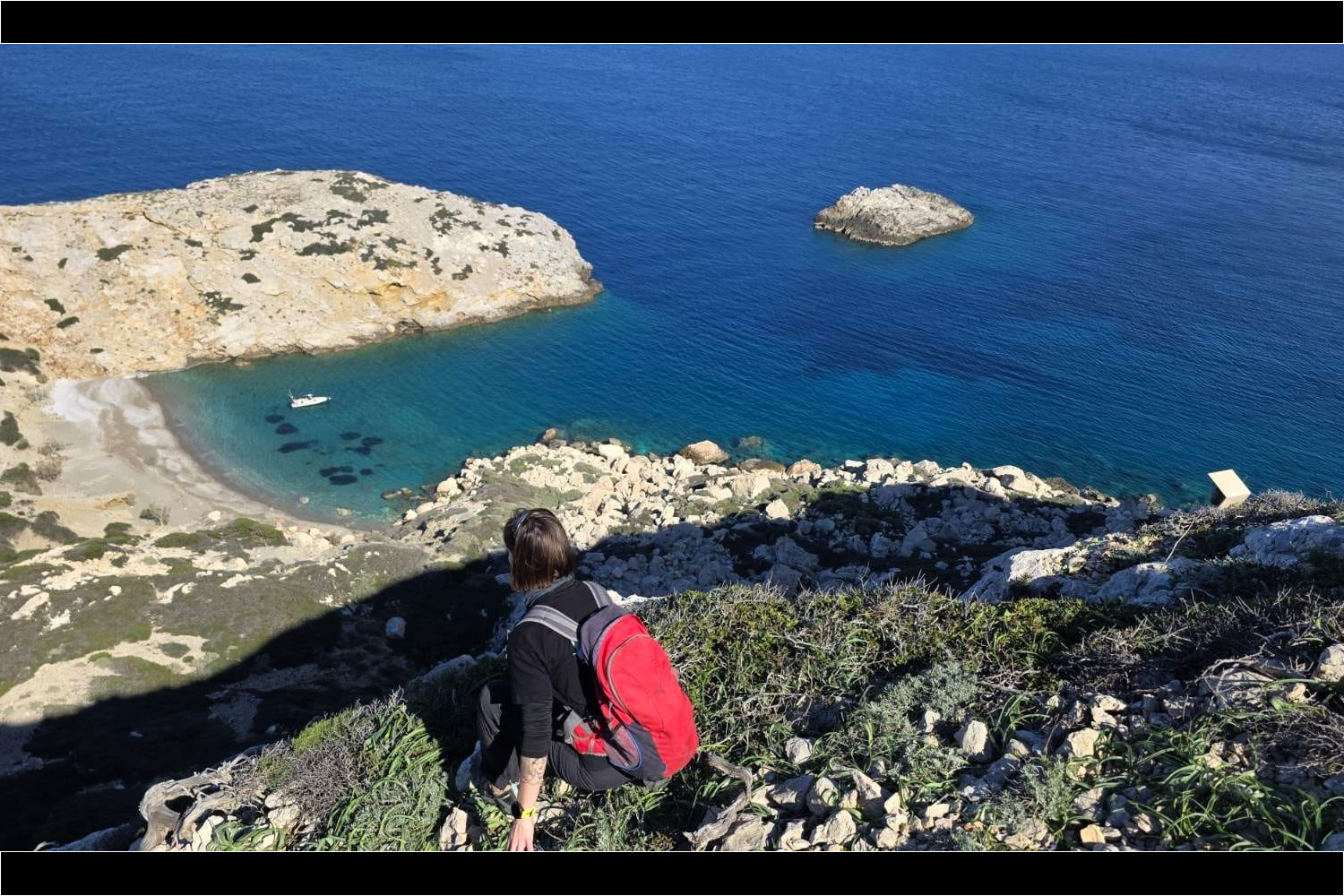 Κοιτάζοντας από την κορυφή βορειοανατολικά μπρος το λιμανάκι στο ανατολικό πλευρό του νησιού, όπου είναι αγκυροβολημένο το φουσκωτό της NCC. Μπροστά μας βρίσκεται το γκρεμνό 50 μέτρων.